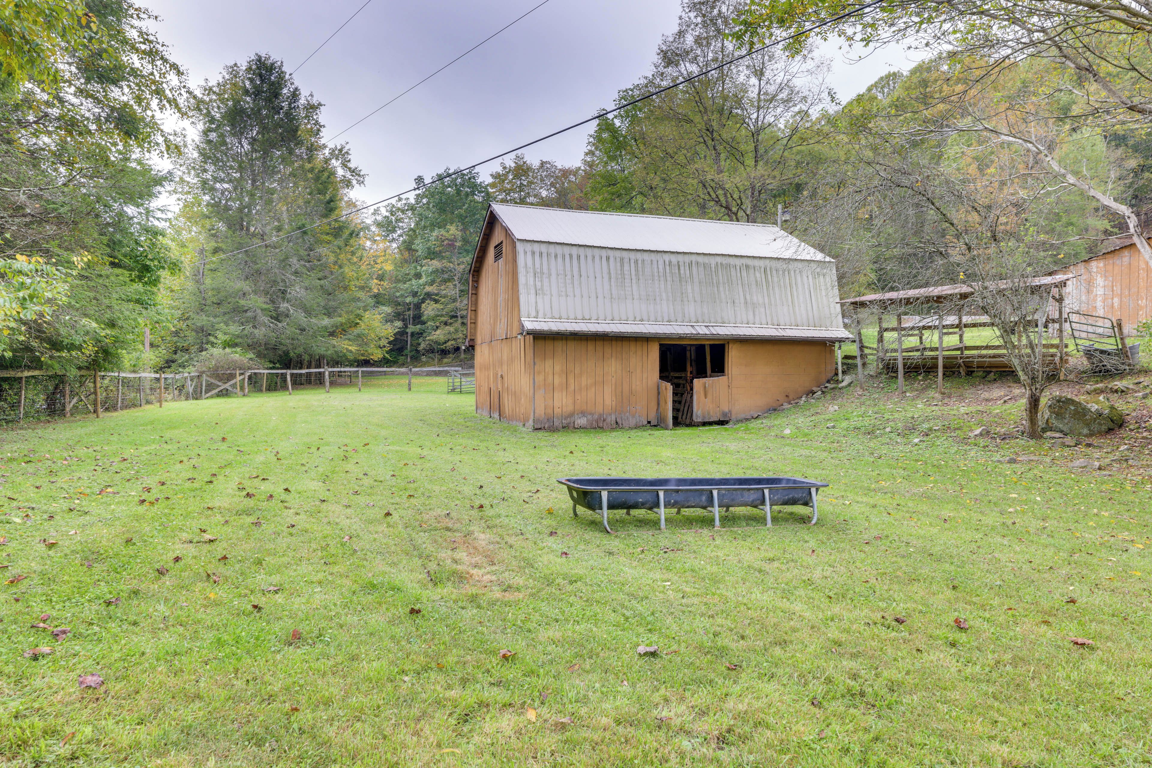 A rustic barn with a sloped roof, surrounded by a fenced pasture and trees.