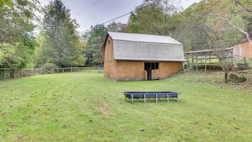 A rustic barn with a sloped roof, surrounded by a fenced pasture and trees.
