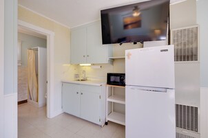Cocina compacta con alacenas blancas, microondas, refrigerador y televisor montado en la pared.