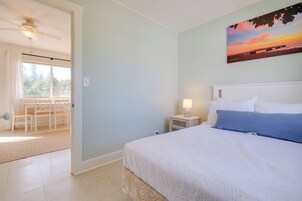 Un dormitorio con una cama, una mesita de noche, una lámpara, un cuadro y vista a un comedor.