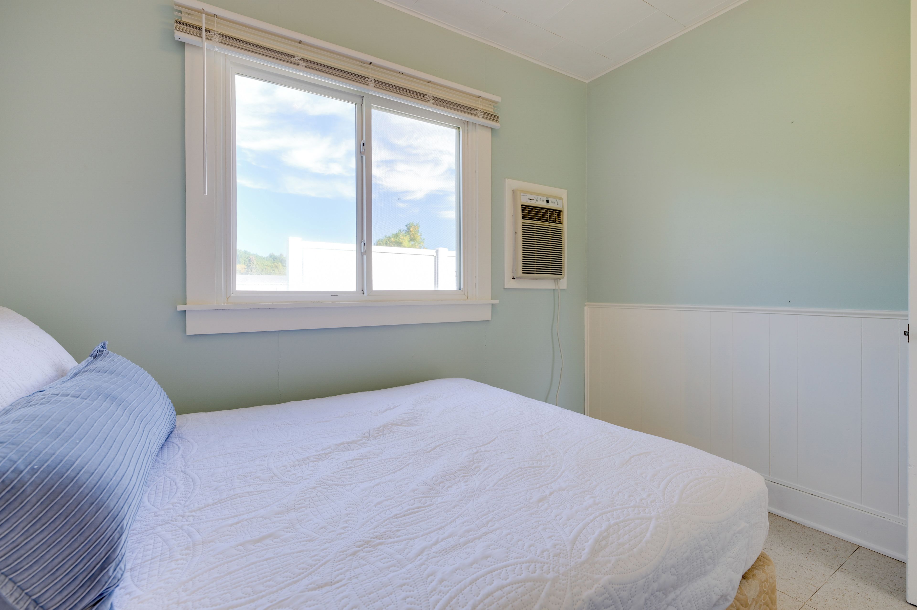 Un dormitorio con cama, ventana y aire acondicionado de pared.