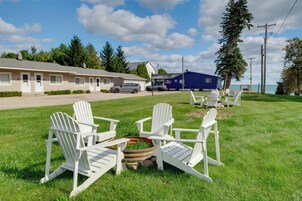 A grassy outdoor area with white Adirondack chairs and a fire pit.