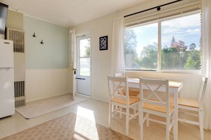 Una habitación con una mesa de comedor, sillas, un ventanal con vistas a árboles y una puerta que da al exterior.