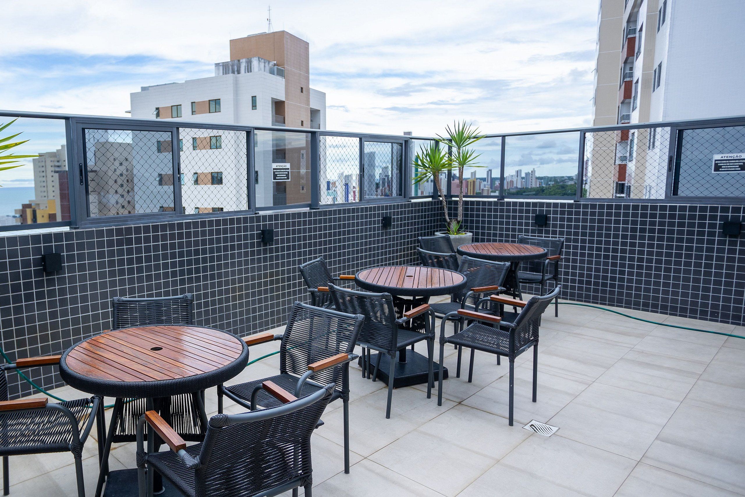 En tagterrasse med runde borde og stole, en potteplante og udsigt over bybilledet.