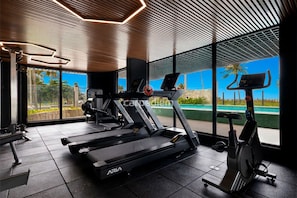Un gimnasio moderno con cintas de correr, una elíptica y una máquina de remo, con ventanas amplias y vistas a una piscina.