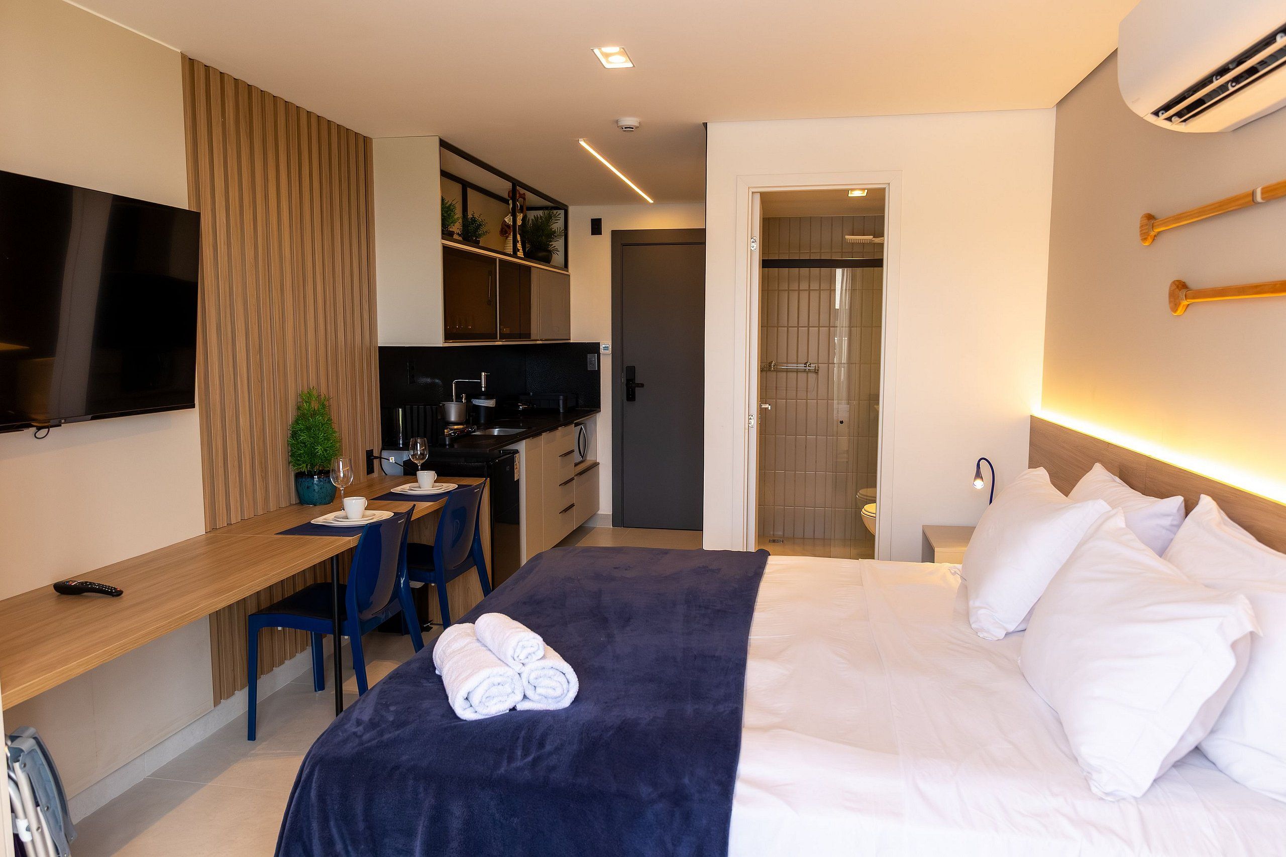 Habitación de hotel con cama, escritorio, televisor, kitchenette y zona de ducha.