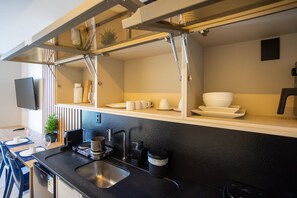 Cocina moderna con encimera negra, pileta de acero inoxidable y horno integrado. Hay una pequeña planta en maceta sobre la encimera y un televisor de pantalla plana montado en la pared.