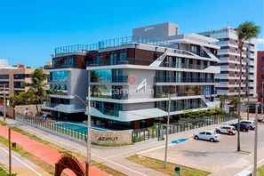 Un hotel de varios pisos con piscina, zona de estacionamiento para automóviles y un llamativo letrero de 'AZIMUT'.