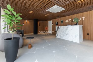 Ein Empfangsbereich mit Holzboden, einer Rezeption, einer Topfpflanze und einem Boden mit Steinmuster.