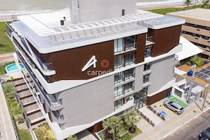 Un edificio moderno de varios pisos con terraza en la azotea, piscina y estacionamiento.