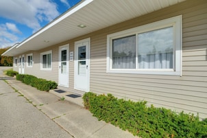 A row of single-story mobile homes with individual front doors and windows, a paved driveway, and a hedge along the side.