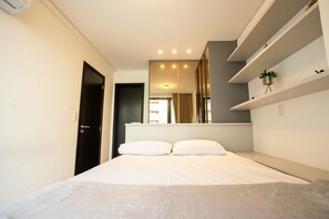 Ein modernes Schlafzimmer mit einem Bett, einer dunklen Tür, einem Spiegel und einem Regal mit einer Pflanze.