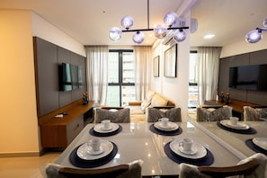 Ein moderner Hotel-Speiseraum mit einem großen Tisch für vier Personen, einer Couch und einem an der Wand montierten Fernseher.