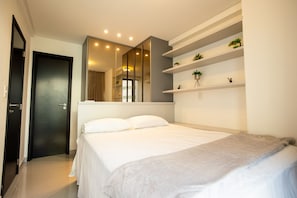 A modern bedroom with a bed, a large mirror, and built-in shelving with plants. - One Way #203 - Tambau Beach by Carpediem (João Pessoa)