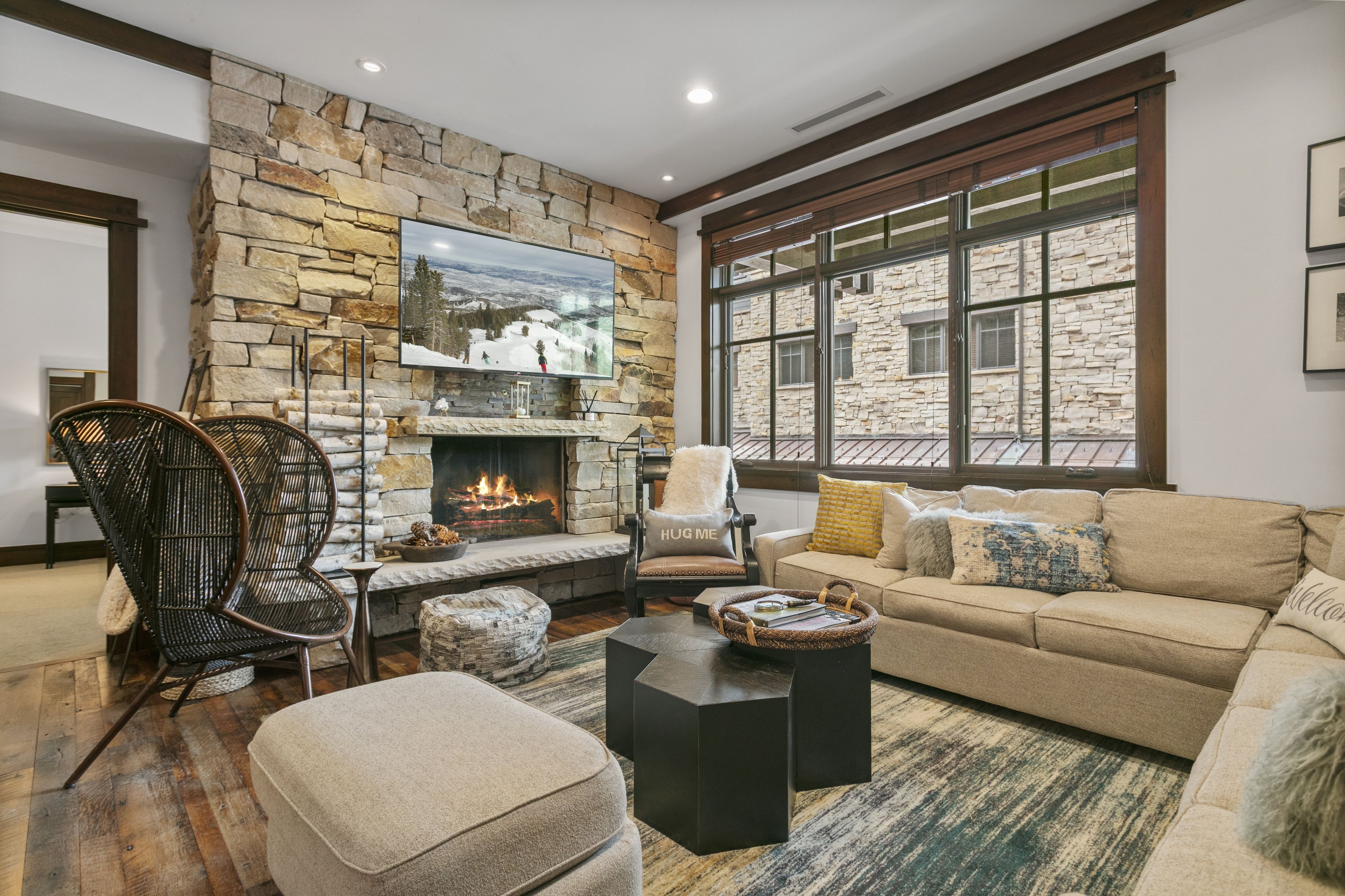 Un salon chaleureux avec une cheminée en pierre, des fauteuils confortables et une grande fenêtre donnant sur l’extérieur.