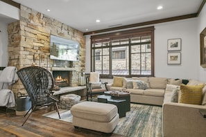 A cozy living room with a stone fireplace, comfortable seating, and a large window. - 201 - Two Bedroom Arrowleaf 2 Condo (Park City)