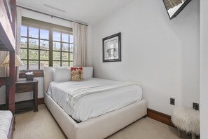 Ein Schlafzimmer mit einem großen Bett, einem Nachttisch, einer Lampe, einem Fenster mit Vorhängen und einem gerahmten Bild an der Wand.