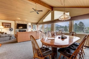 Una sala de estar amplia con chimenea, un comedor con mesa redonda y grandes ventanas que ofrecen vistas al exterior.