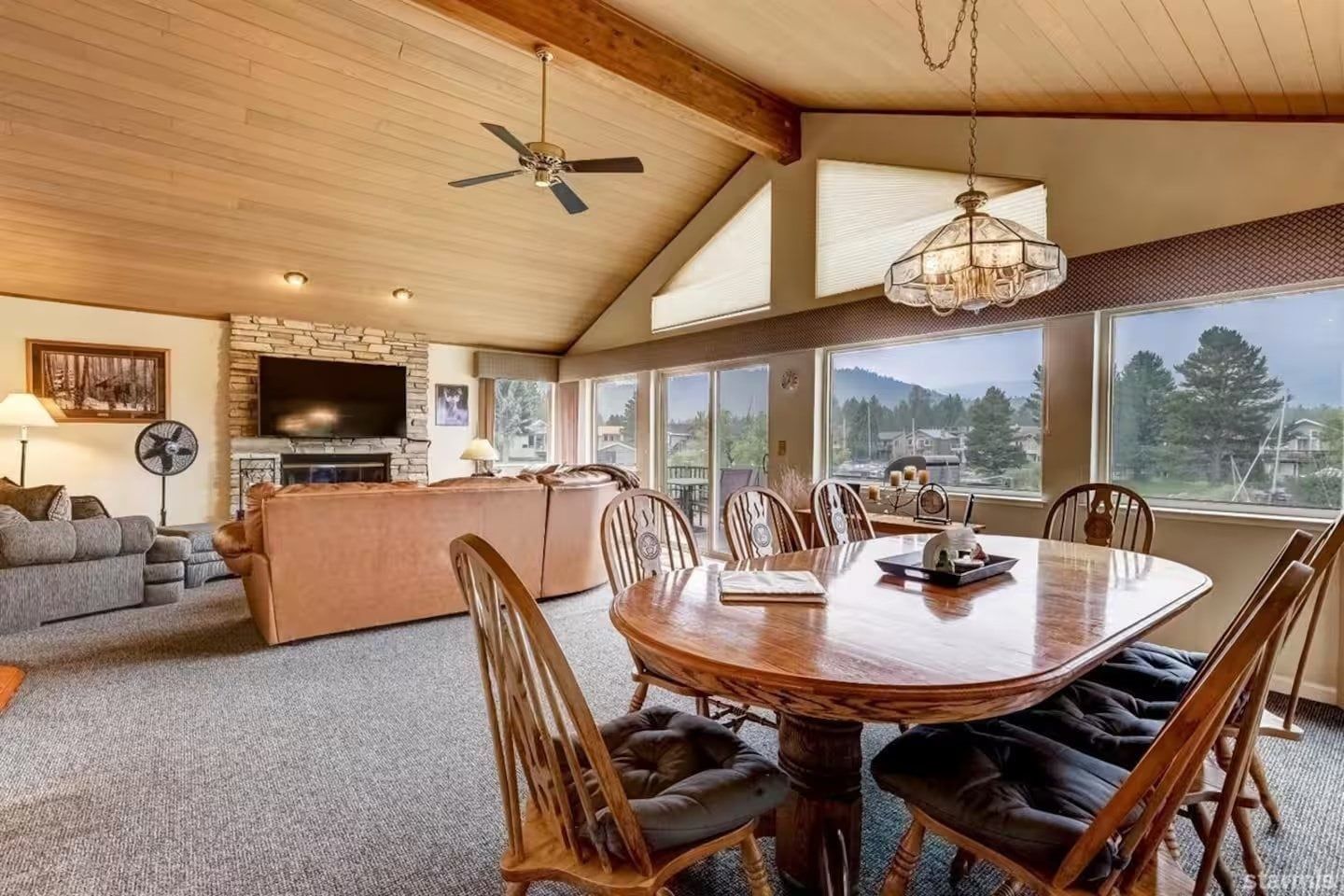 Uma sala de estar ampla com lareira, área de jantar com mesa redonda e grandes janelas com vista para o exterior.