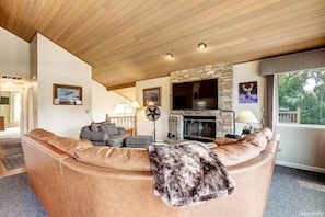 A modern living room with a stone fireplace, leather sofa, and a television. - 546 Alpine Drive 3 Bedroom Home (South Lake Tahoe)
