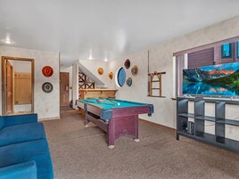 Una habitación con mesa de billar, televisión y sofá azul.