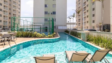Una piscina con baldosas a cuadros, rodeada de sillas de descanso y un pequeño jardín.