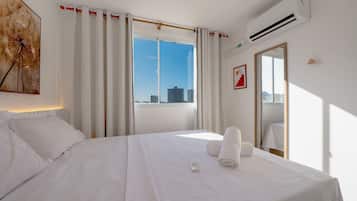 Habitación de hotel con cama, ventana con cortinas, aire acondicionado y vistas a la ciudad.