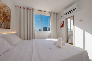Ein Hotelzimmer mit Bett, Vorhängen am Fenster, einer Klimaanlage und Blick auf die Stadt.