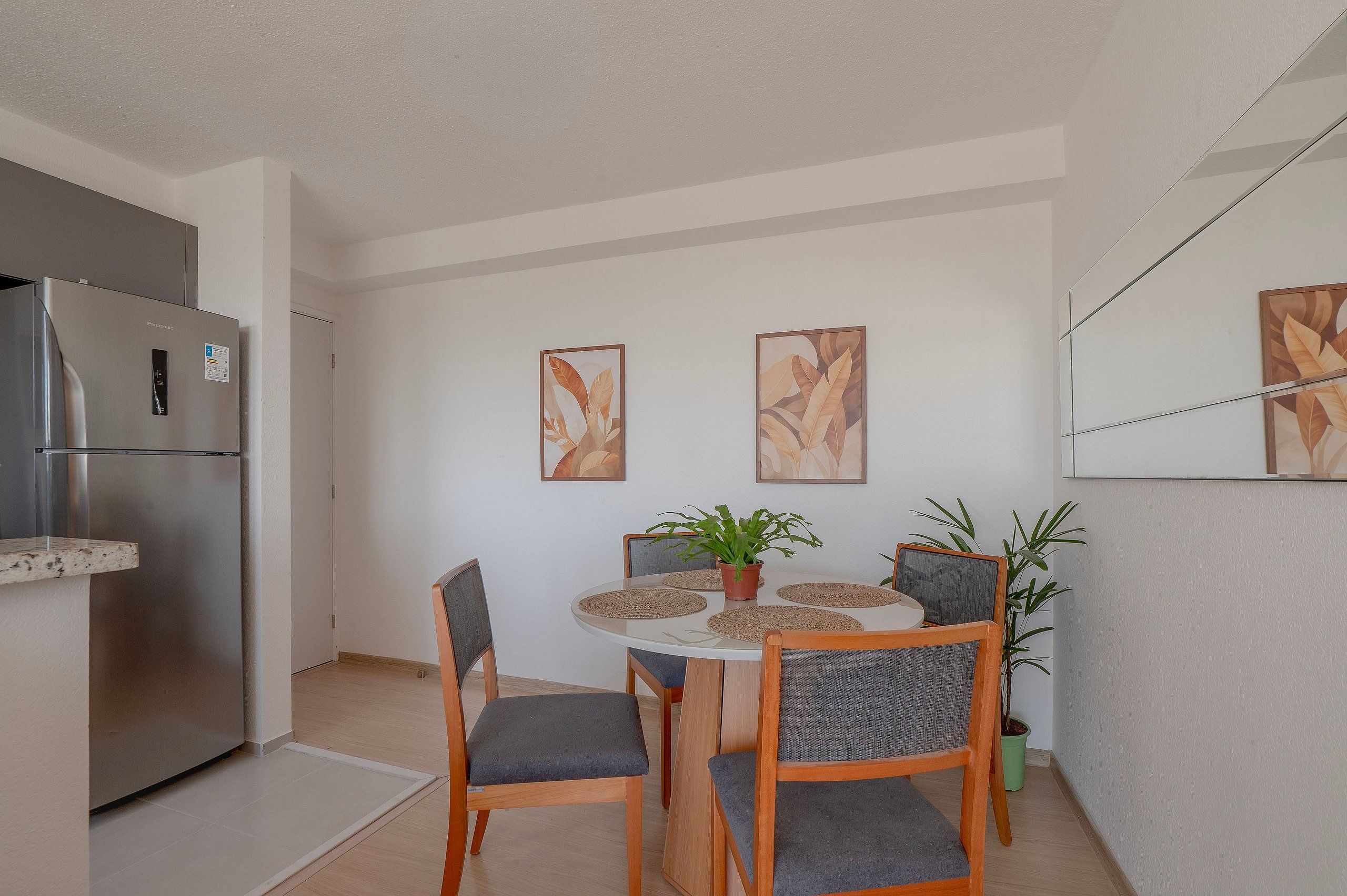 A compact kitchen with a built-in refrigerator, a dining table with four chairs, and two wall-mounted paintings.