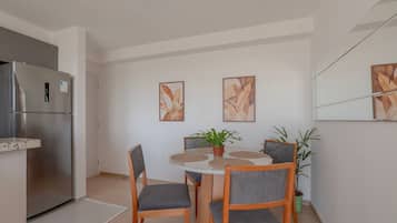 A compact kitchen with a built-in refrigerator, a dining table with four chairs, and two wall-mounted paintings.