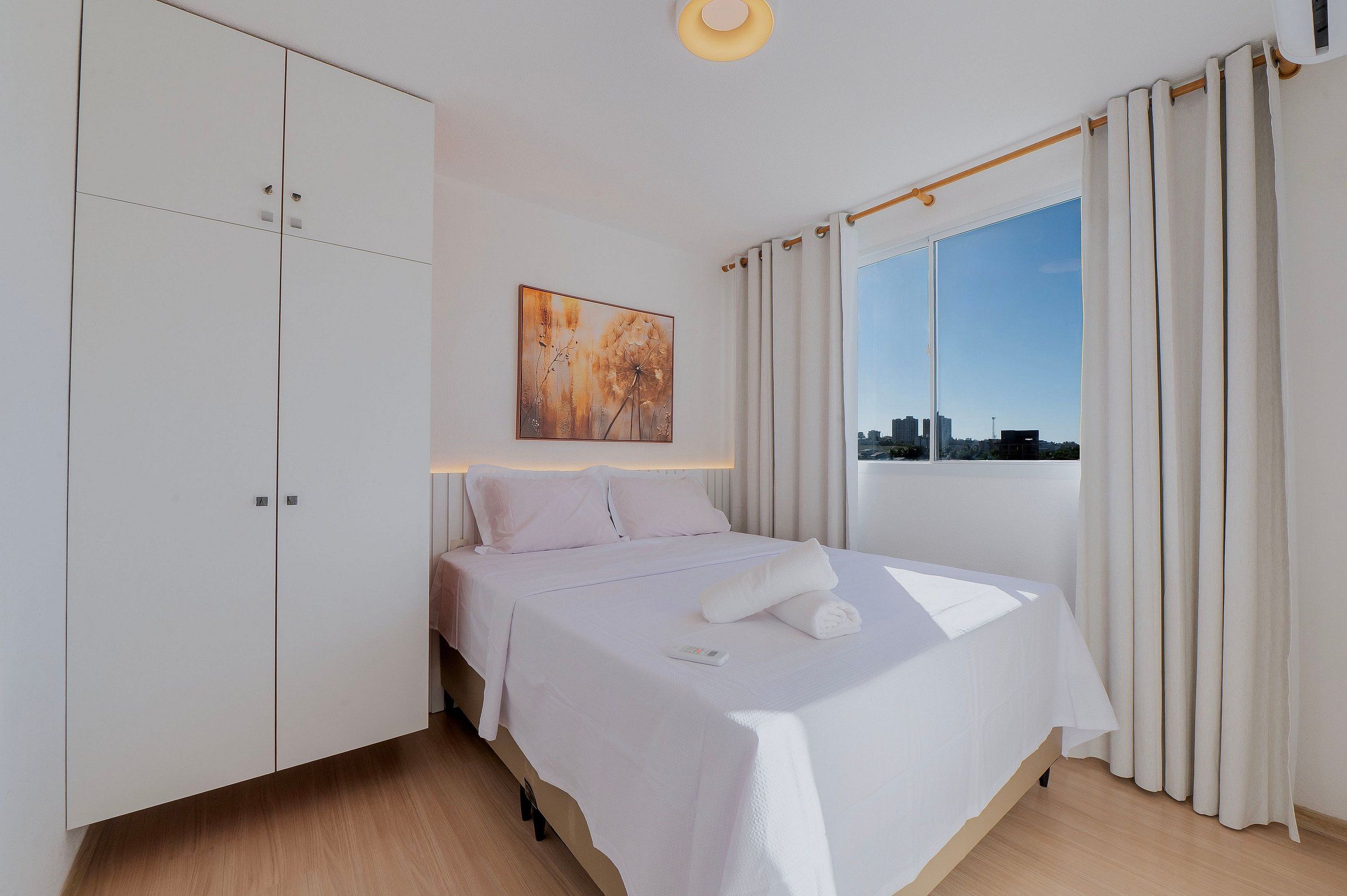 Ein Hotelzimmer mit Bett, Kleiderschrank, einem Fenster mit Vorhängen und Blick auf die Stadt.