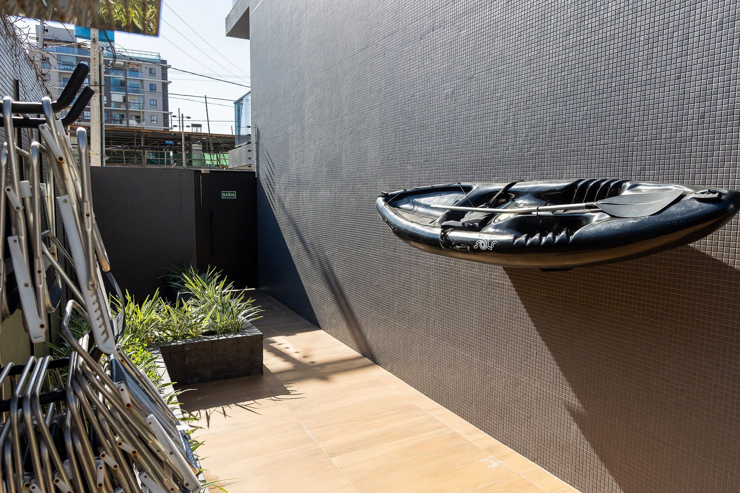 A boat mounted on a textured wall, a metal rack with pipes, and a small planter with plants.