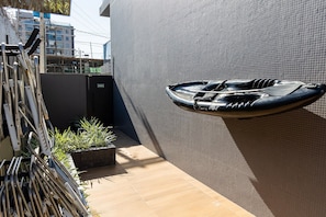 Um barco fixado numa parede com textura, uma estante de metal com tubos e um pequeno vaso de plantas.