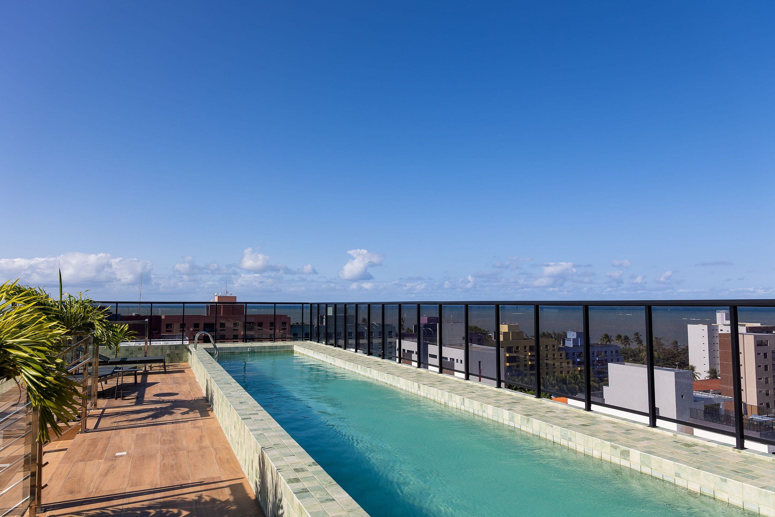 A rooftop swimming pool with a clear view of the cityscape and ocean in the background.