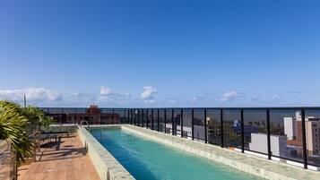 A rooftop swimming pool with a clear view of the cityscape and ocean in the background.