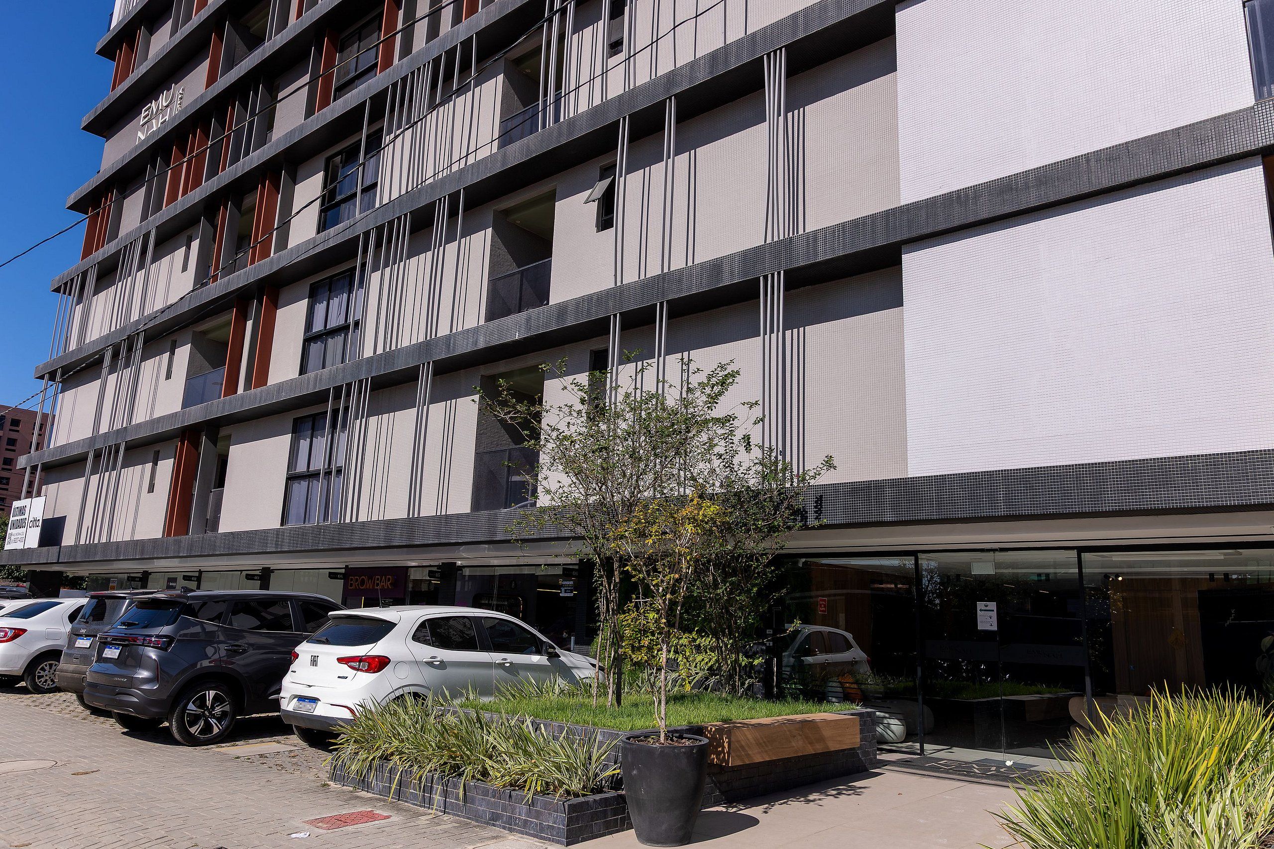 A multi-story hotel with a modern facade, parking area, and a small tree in the foreground.