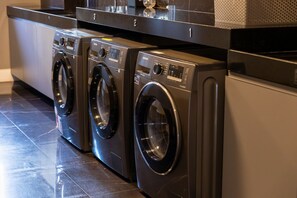 A row of black front-loading washers with control panels, placed on a tiled floor. - Mardisa Design #705 in Cabo Branco by Carpediem (João Pessoa)