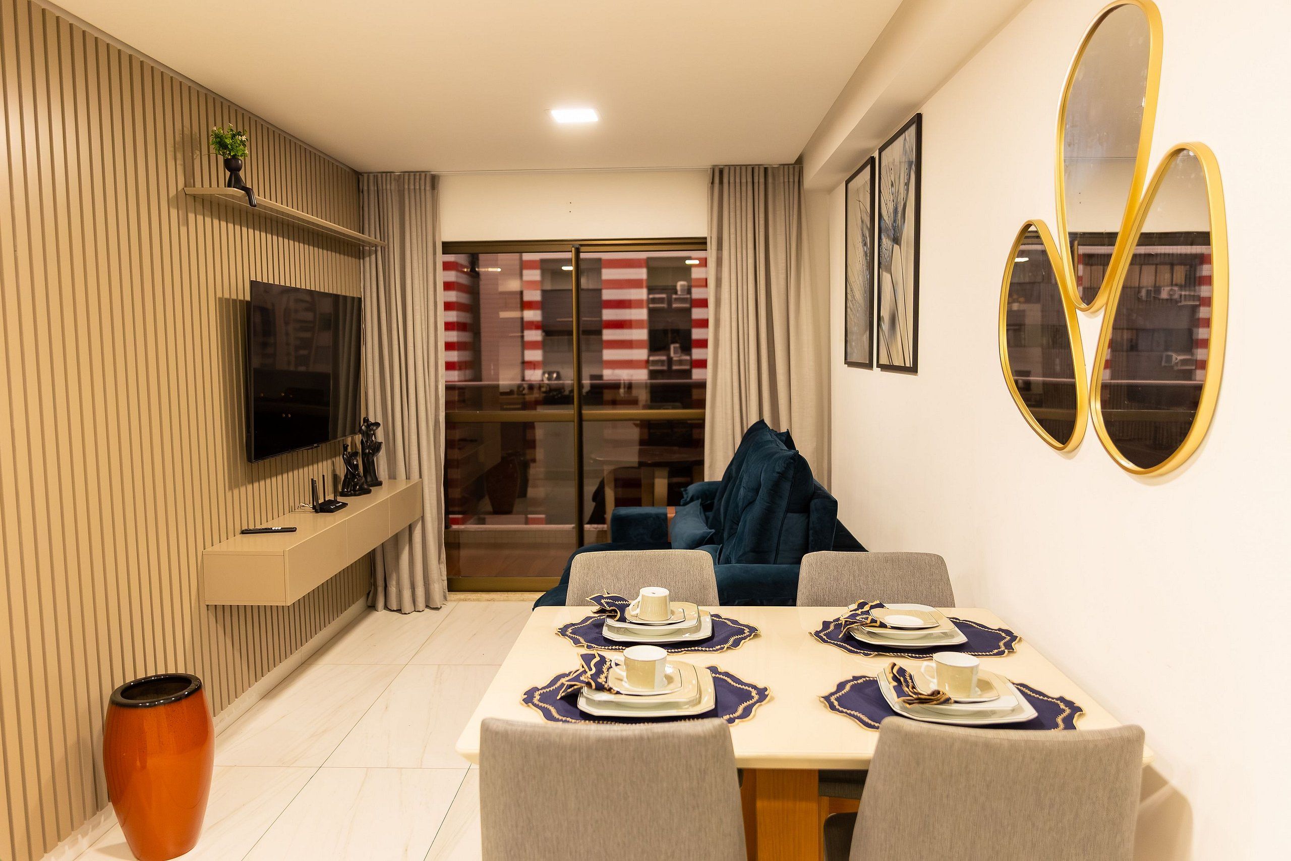 Zona pranzo moderna con TV a parete, divano e tavolo imbandito con piatti e tazze.