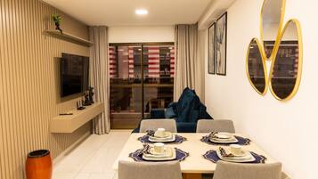 Zona pranzo moderna con TV a parete, divano e tavolo imbandito con piatti e tazze.