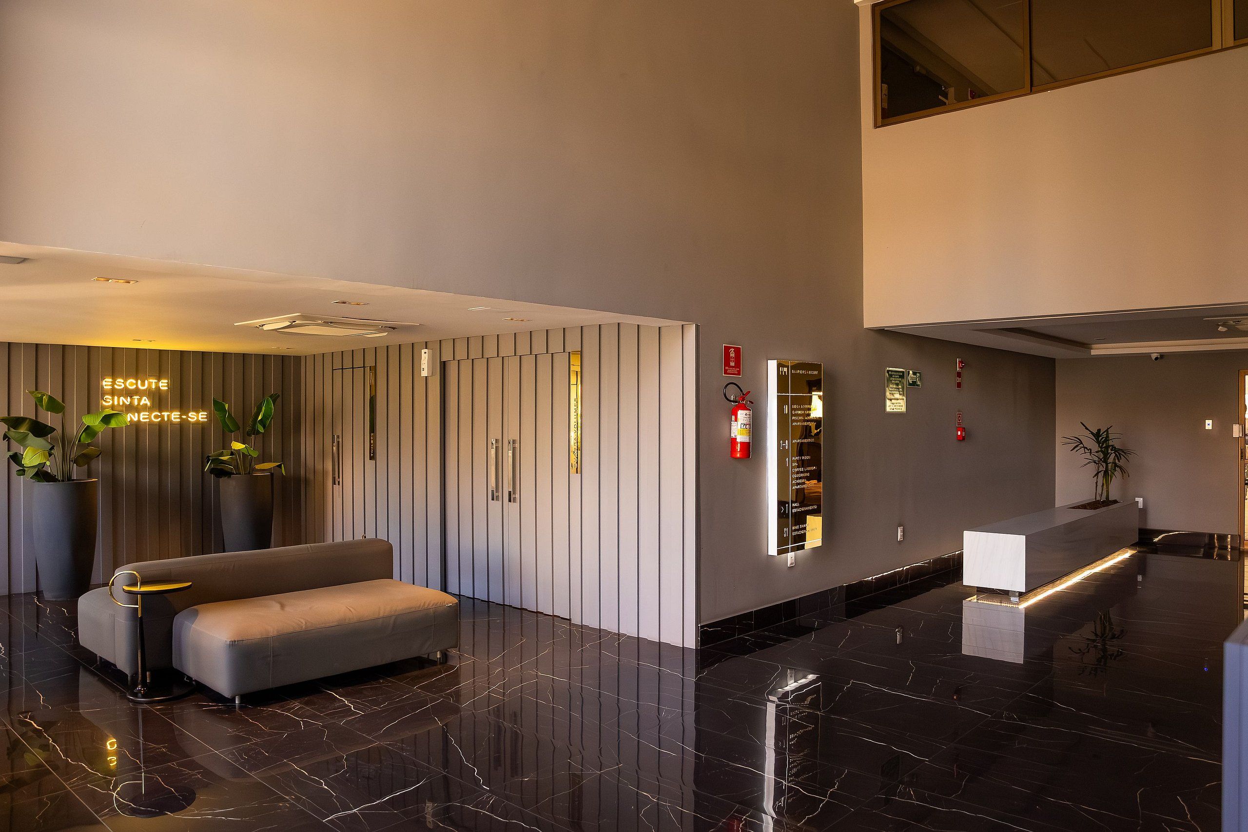 Una hall moderna con reception, area salotto e segnaletica direzionale.
