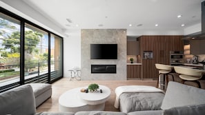 A modern living room with a fireplace, a flat-screen TV, and a dining area with bar stools. - The Venice Modern in Venice (Venice)