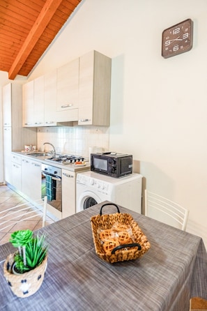 A compact kitchen with a microwave, stove, and washing machine, a dining table with a basket, and a small potted plant. - defaultName (Piedimonte San Germano)