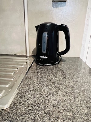Een zwarte waterkoker op een granieten aanrecht met een metalen dienblad links ervan.