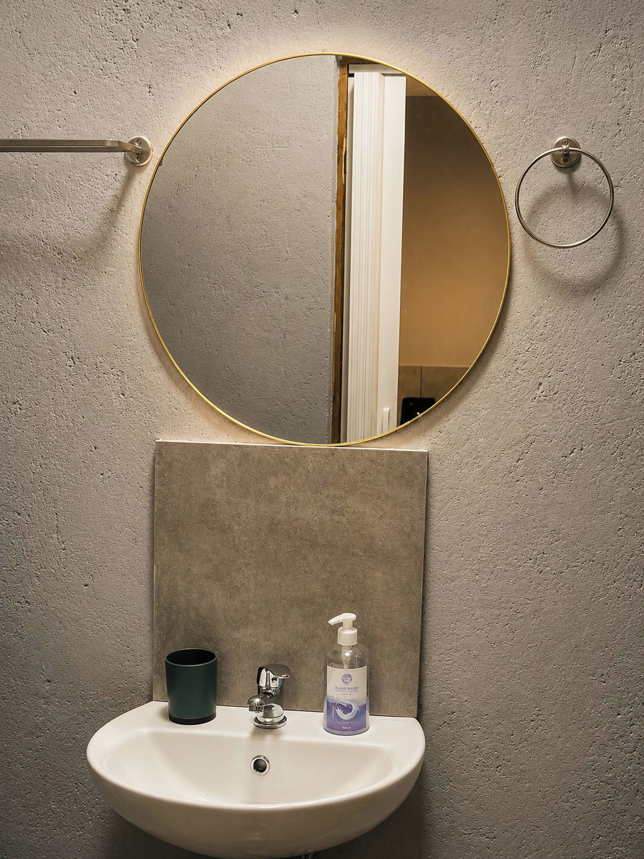 A bathroom with a round mirror, a sink, a soap dispenser, and a towel ring.