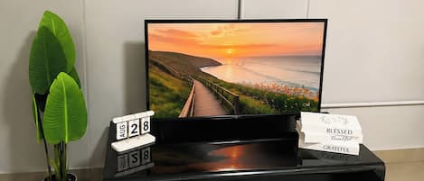 Ein Flachbildfernseher auf einer schwarzen Unterhaltungsanlage mit Datumsanzeige und einer Pflanze daneben.