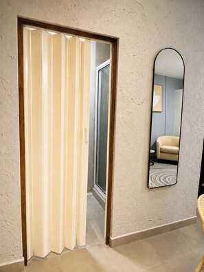 Ein Zimmer mit einer Schiebetür, die zu einem Flur führt, einem Spiegel an der Wand und einem Korbstuhl.