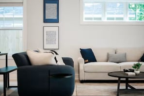 Ein modernes Wohnzimmer mit einer Couch, Sesseln, einem Couchtisch und gerahmten Kunstwerken an der Wand.