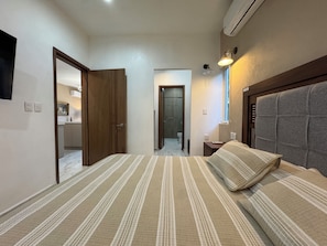 A bedroom with a bed, a nightstand, a lamp, and a view of the bathroom. - Palms Reef - Peaceful Condo with Pool & Steps to Beach (Cozumel)