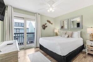 Un dormitorio con una cama grande, una mesita de noche, una silla, un ventilador de techo y vistas de edificios a través de la ventana.