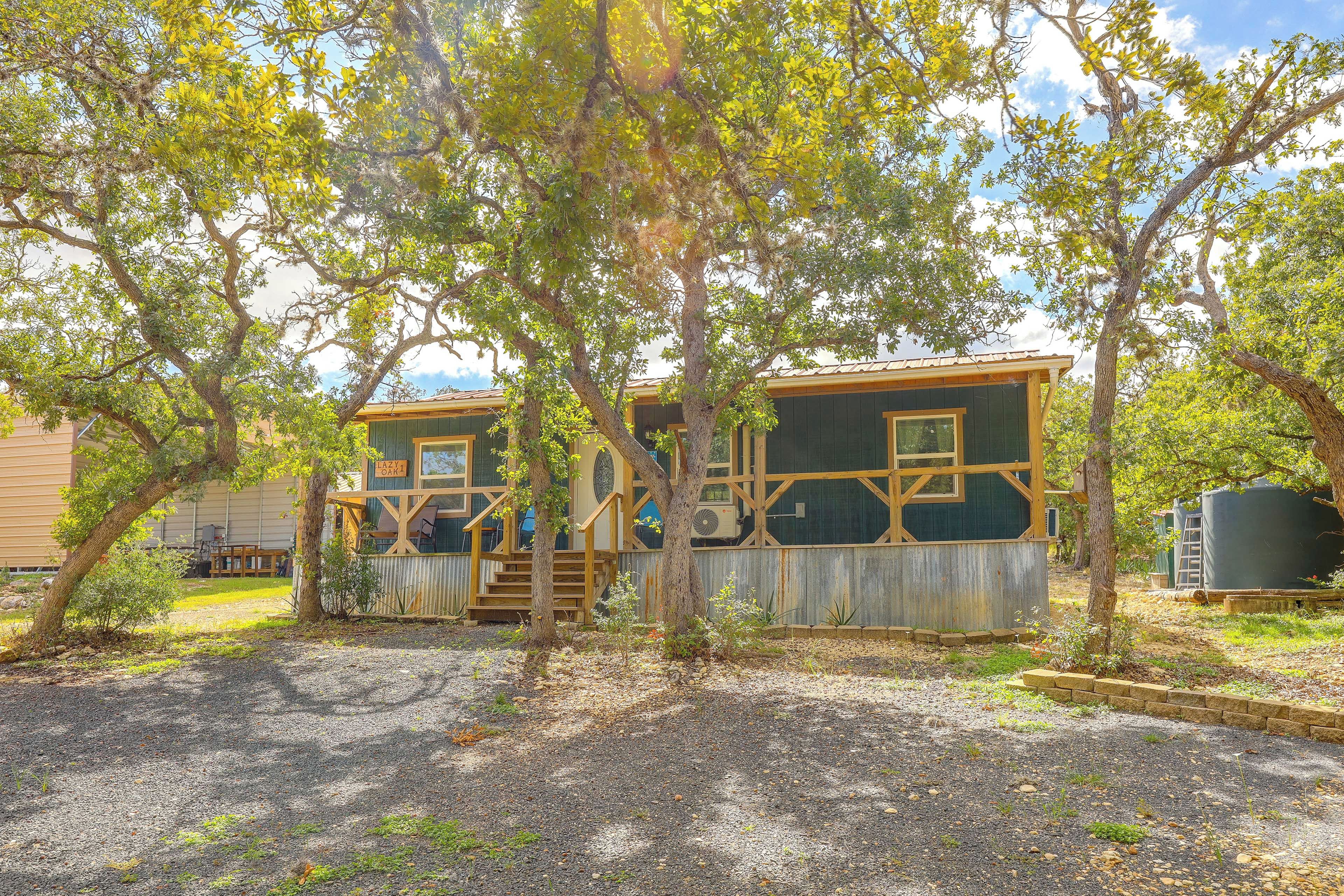 A rustic cabin with a wooden deck and a large window, surrounded by trees.